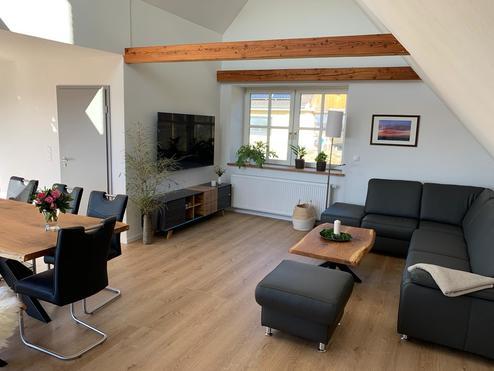 Helles Wohnzimmer mit Holzboden Freundlich eingerichtetes Wohnzimmer mit schwarzem Ledersofa, Holzboden und offenem Essbereich mit Holztisch.