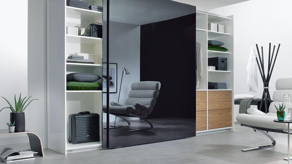 Wohnraumimpression mit abgetrennter Ruheoase Wohnraumimpression mit abgetrennter dunkler Glasschiebetür für Ruheoase und integrierten Einbauregalen